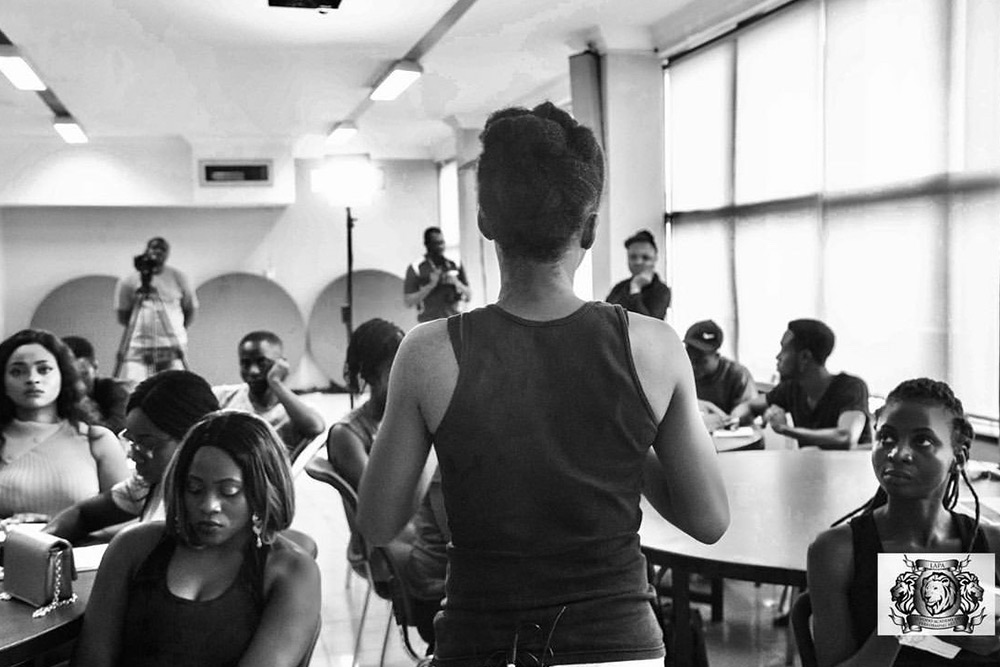 A black-and-white workshop circle, a student standing to deliver while the group watches.