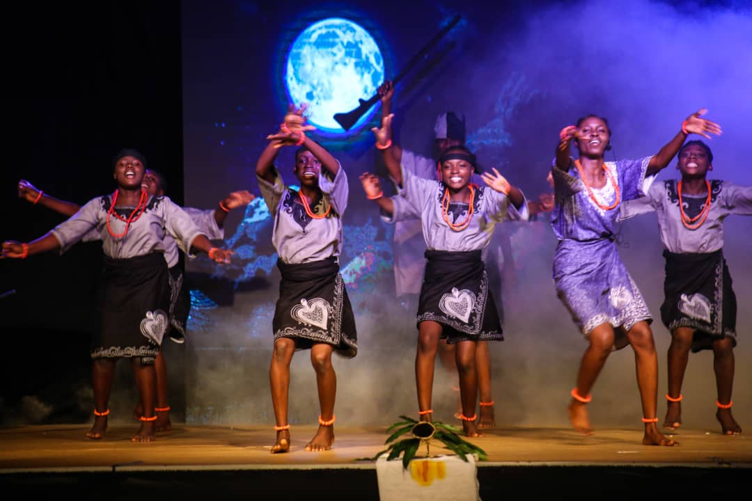 Students performing on a lit stage against a moon backdrop.