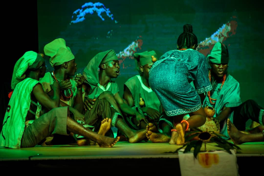 An ensemble in green stage light, mid-choreography.